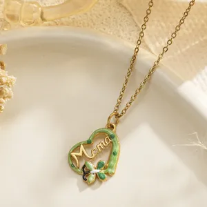 Detail shot of a gold heart pendant with green enamel and Mama script engraving.