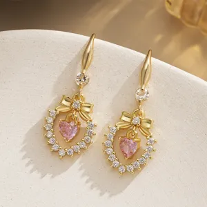 Close-up detail of gold-plated earrings featuring pink heart zircon and bow design