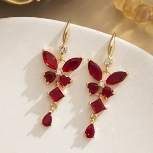 Close-up of vintage gold earrings with red butterfly-shaped zircons on beige stone.