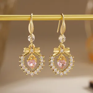 Detailed macro view of gold-plated bow earrings featuring a pink heart-shaped zircon center