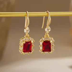 Close-up of elegant gold drop earrings with emerald-cut red zircon and crystal halo