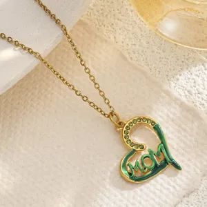 Macro detail of a gold heart pendant necklace featuring green enamel and MOM engraving