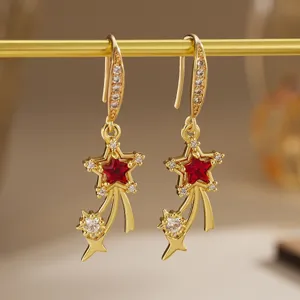 Detailed macro of gold star earrings featuring vibrant red zircon and shooting stars.