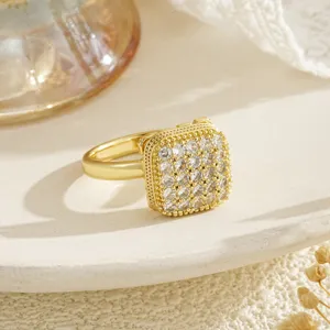 Detailed view of a golden rotatable square ring with shimmering zircons on white plate
