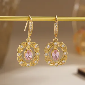 A detailed macro view of gold-plated earrings with pink zircon and filigree work