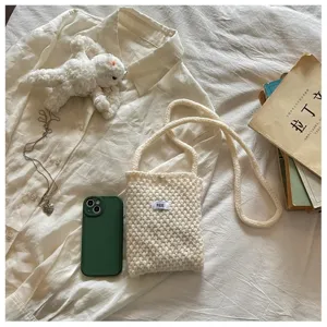 Cream white knitted crossbody phone bag featuring a minimalist egg tag on white fabric