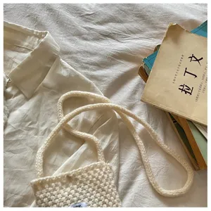 Detail view of cream knitted crossbody phone bag with soft texture on white bedding