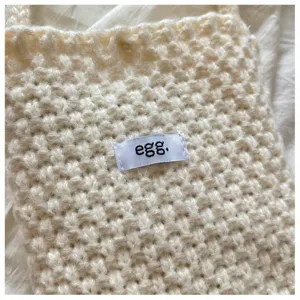 Macro close-up of a cream knitted phone bag with 'egg.' label showing soft texture