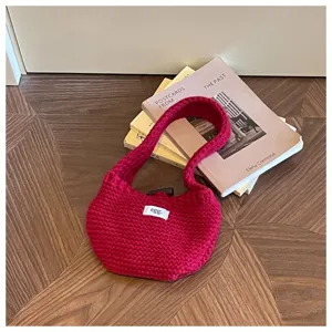 Close-up of a red knitted wool handbag styled with books on a wooden floor