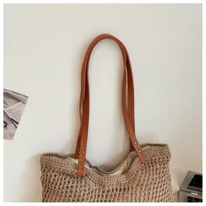 Close-up detail of a hand-woven straw beach bag with durable orange leather shoulder straps.
