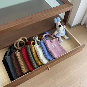 Handmade knitted mini crossbody phone bags in various candy colors organized in a drawer.