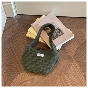 Close-up of a chunky dark green knitted handbag with egg. label resting on books