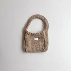 Detailed close-up of a cozy beige knitted wristlet bag with a small 'egg.' label