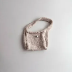 Close-up of a beige chunky knit wrist bag featuring a minimalist 'egg.' fabric tag