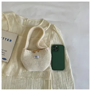 Detailed view of a cream knitted mini handbag next to a phone for size reference