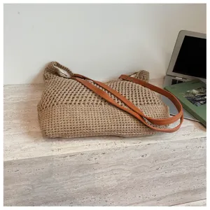 Detail view of a beige woven cotton beach bag with tan leather straps on a table.