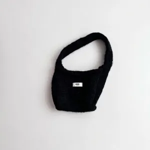 Detail view of a minimalist black knitted wrist bag with a white 'egg.' brand label