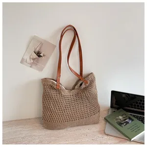 Detail of a beige crochet woven tote bag with brown leather straps in a lifestyle setting.