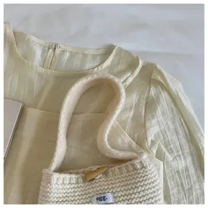 Close-up view of a minimalist cream knitted mini handbag featuring a wooden toggle button