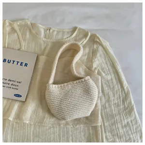 Detailed view of a chic white knitted handheld mini bag on cream pleated fabric background