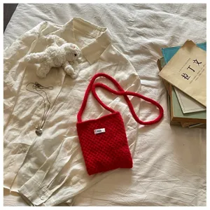 Macro detail of a bright red knitted crossbody phone bag featuring a minimalist egg tag