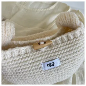 Close-up of a cream knit handbag showing the wooden toggle button and tag detail.