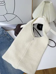 Detail of cream white knitted tote bag with minimalist logo and coarse knit texture
