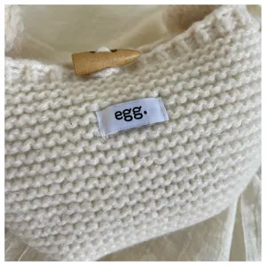 Close-up of white knitted wool handbag featuring a toggle button and egg. fabric label