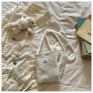 Close-up of a white knitted crossbody bag with egg. label resting on a soft beige shirt
