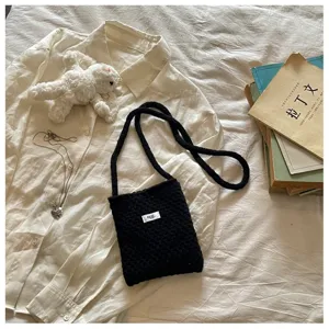 Close-up of black knitted crossbody phone bag on white shirt with vintage book props
