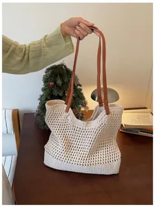 Detail of cream hollowed-out knitted tote bag with brown leather handles in cozy setting