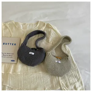 Detail view of small knitted handbags in charcoal and cream colors with egg labels