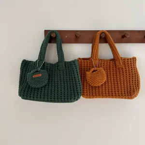 Two handmade crochet tote bags in green and brown hanging on a wooden rack