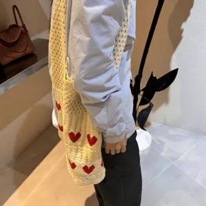 Detailed view of cream knitted tote bag with red heart pattern on model's shoulder