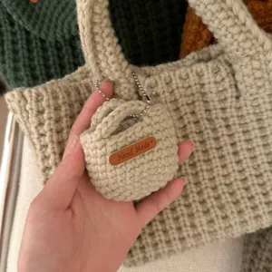 Detail of a handmade cream cotton crochet mini pouch with leather tag and chain