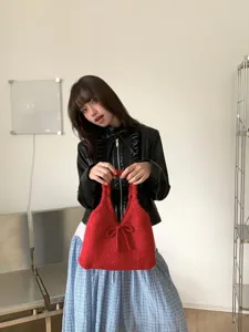 Fashionable Asian model showcasing a red knitted handbag featuring a cute bow detail