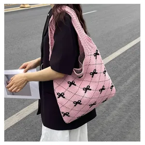 Close-up of a pink knitted tote bag with black bow patterns worn outdoors on a street