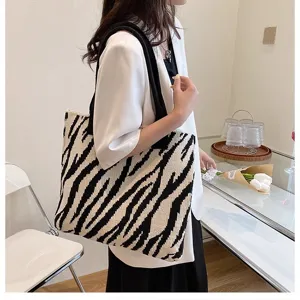 Lifestyle detail view of a large zebra-print knitted tote bag carried by a model