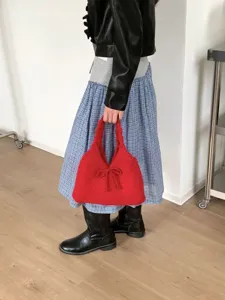 Detailed shot of a bright red knitted tote bag with bow accent held by a casual model