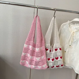 Close-up detail of heart pattern crochet knit tote bags in pink and white hanging on a rack
