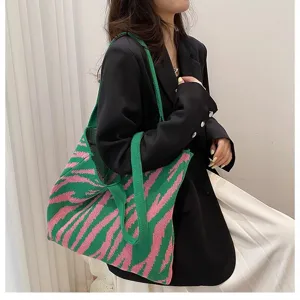 Large knitted tote bag with pink and green zebra pattern carried by a model