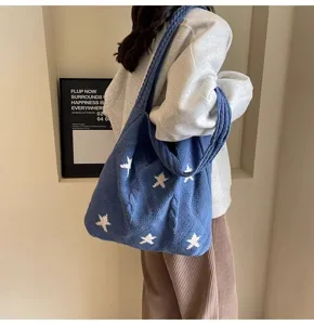 Blue knitted star pattern tote bag being worn by a model in a minimalist setting.