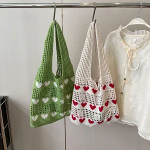 Hand-knit hollow tote bags featuring a sweet heart pattern hanging on a clothing rack