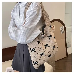 Stylish beige knitted tote bag with black bow patterns shown worn over the shoulder