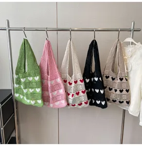 Detailed view of various colors of heart hollow knit tote bags hanging on a rack