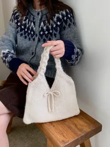 Detailed view of a cream knitted handbag featuring a delicate bow accent on a wooden bench