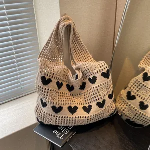 Close-up of a beige knitted tote bag with black heart patterns and mesh design