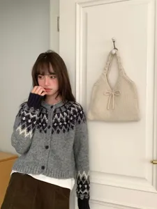 Detail showing a stylish cream knitted tote bag with bow hanging on a white door