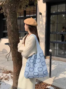 Dettaglio di una borsa tote in maglia blu con motivo a cuori indossata da una modella