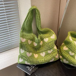 Close-up of green knitted tote bag featuring white heart patterns and hollow-out design.